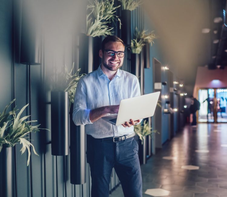Half length portrait of successful boss using netbook technology with 4g wireless internet connection in workspace interior, prosperous employee in classic eyewear holding laptop computer and smiling Half length portrait of successful boss using netbook technology with 4g wireless internet connection in workspace interior, prosperous employee in classic eyewear holding laptop computer and smiling